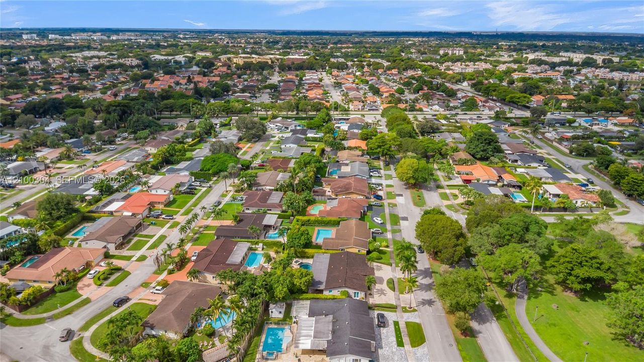 Aerial perspective of a suburban neighborhood featuring residential dwellings, established tree canopy, paved roadway infrastructure, and integrated community green space