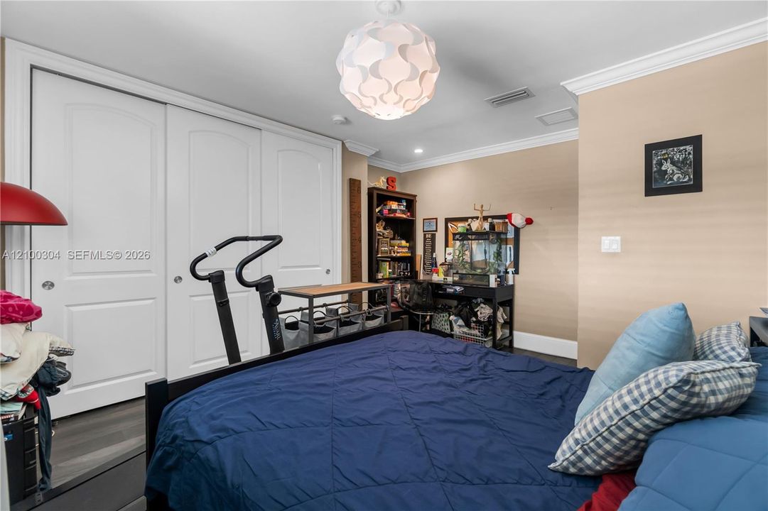 Room featuring crown molding, neutral wall finishes, wood-finish flooring, and a large closet with three-panel doors