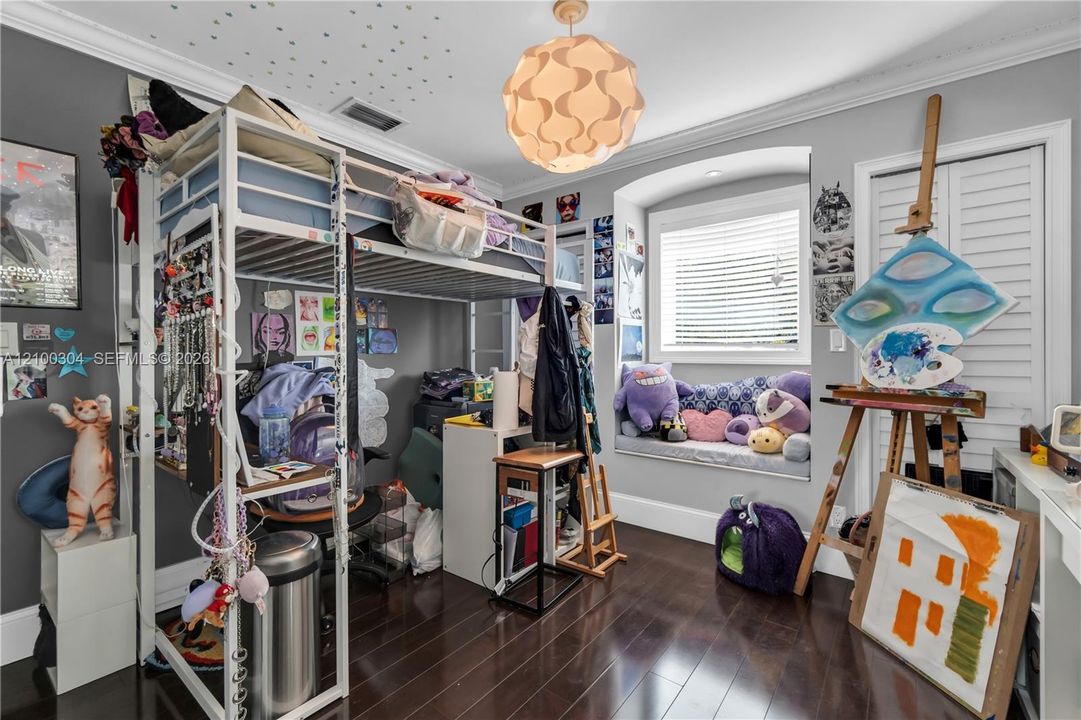 Room featuring wood-finish flooring, a built-in window seat, crown molding, double-louvered closet doors, and a decorative pendant light fixture