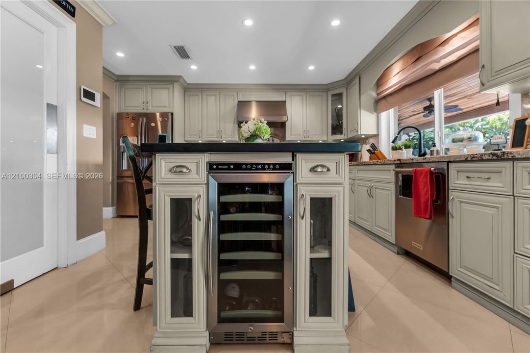 Kitchen featuring painted wood cabinetry, center island with integrated wine refrigerator, stainless steel appliances, and solid surface countertops