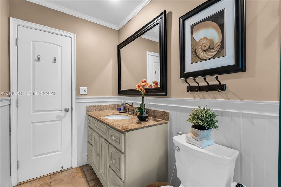 Bathroom featuring a vanity with stone-finish countertop, undermount sink, wainscoting, framed wall mirror, and crown molding