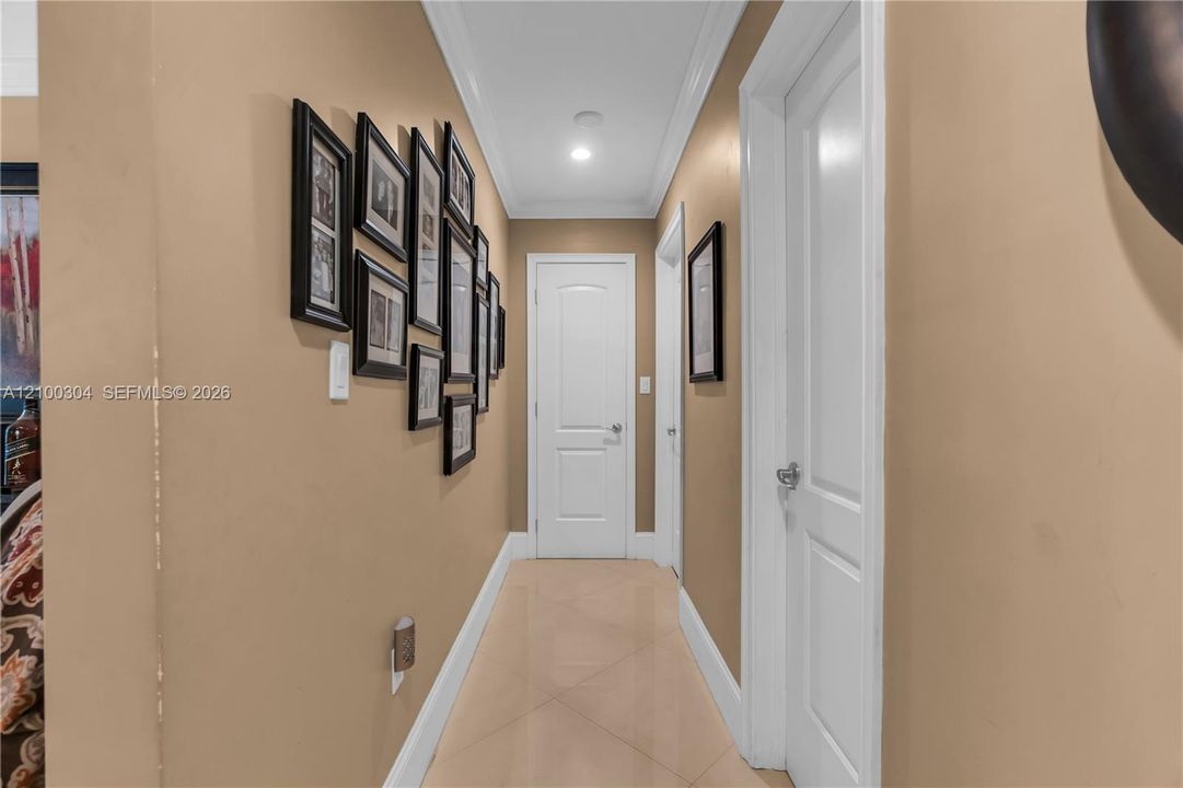 Interior hallway featuring large-format tile flooring, crown molding, recessed lighting, and multi-panel interior doors with brushed nickel hardware