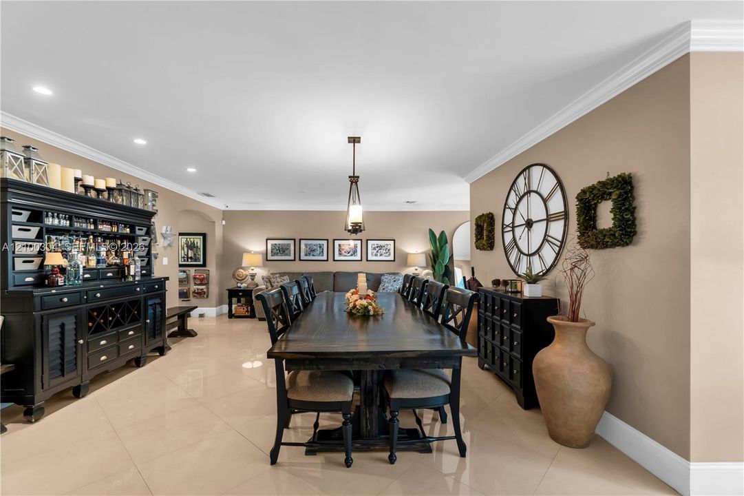Open-concept space featuring polished tile flooring, recessed lighting, crown molding, a built-in cabinetry unit, and a central pendant light fixture