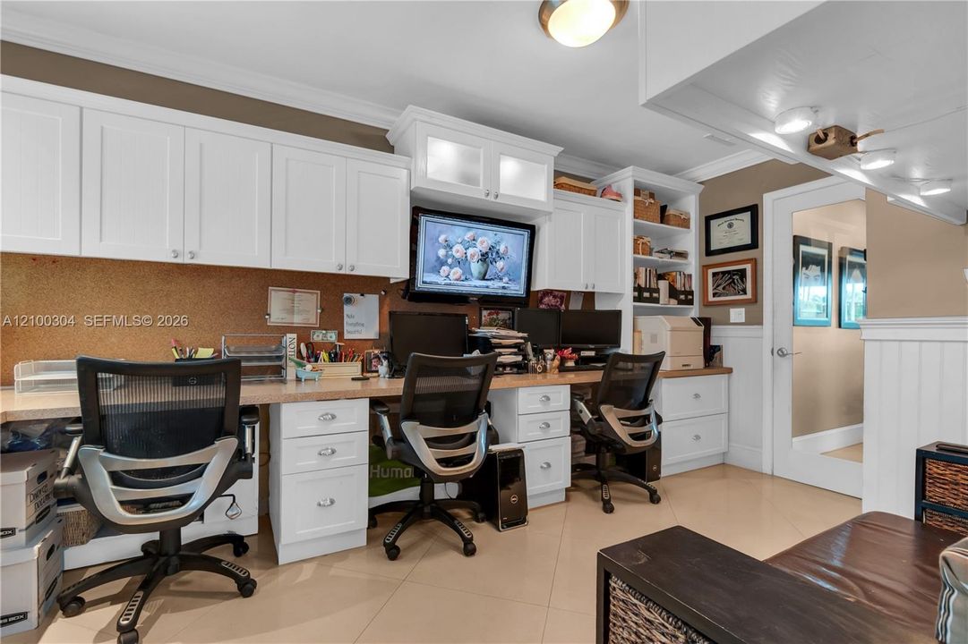 Built-in workstation featuring white cabinetry with frosted glass accents, extensive drawer storage, open shelving, and a continuous work surface