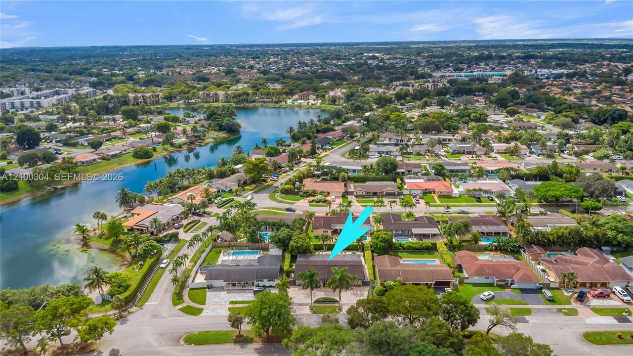 Aerial perspective of a residential property featuring a paved driveway, a multi-car garage, mature palm trees, and proximity to a central lake