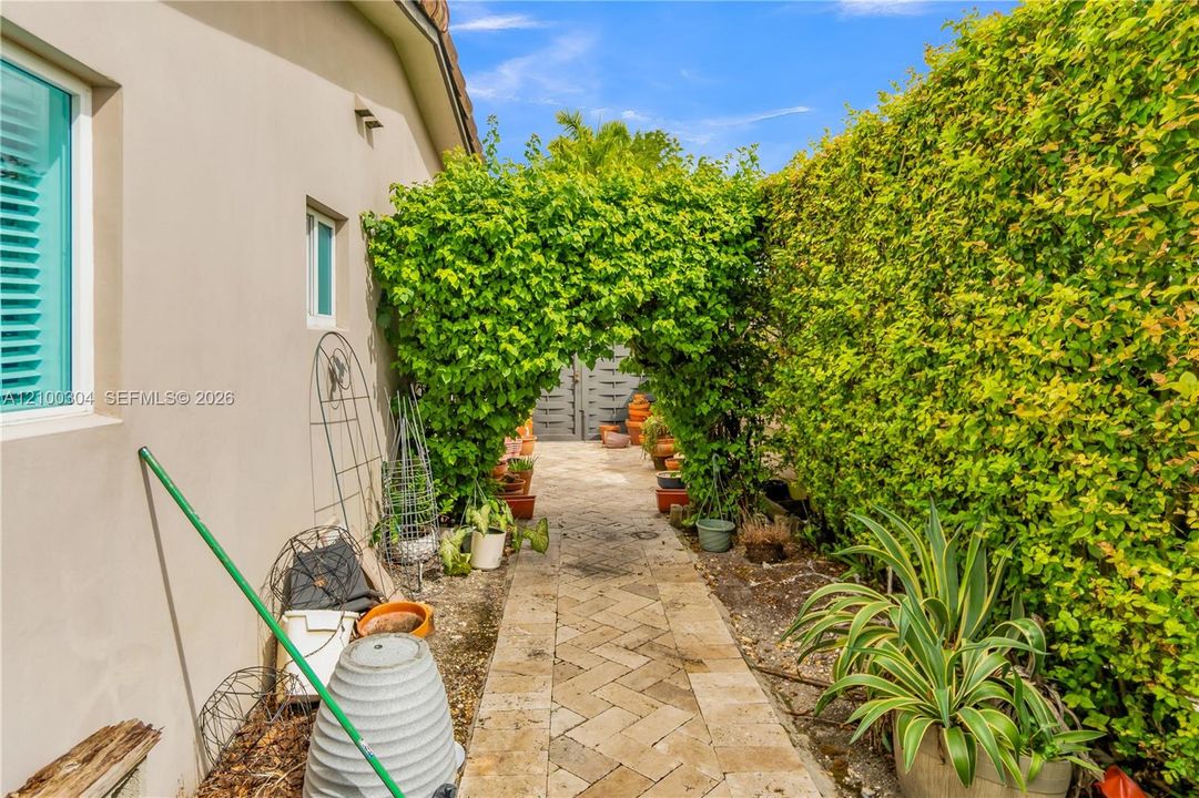 Herringbone-patterned stone paver walkway bordered by high privacy hedges and a foliage-covered archway