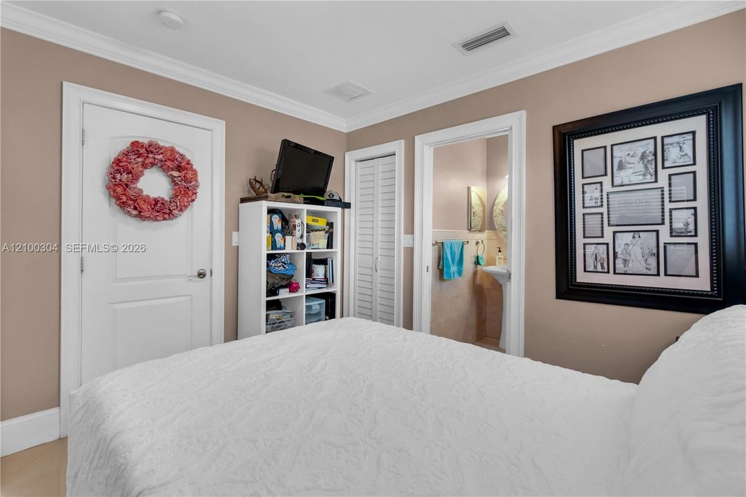 Neutral interior featuring white two-panel doors, white louvered closet doors, crown molding, and a pedestal sink