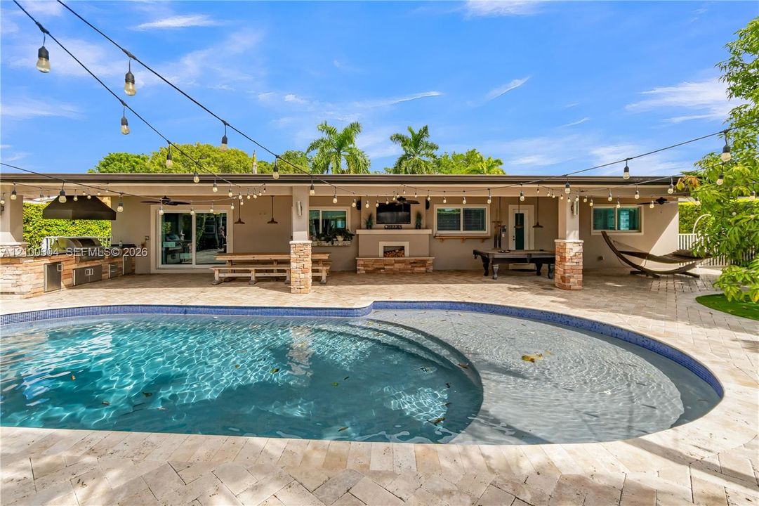 Expansive covered patio featuring natural stone flooring, a built-in outdoor kitchen, a stone-clad fireplace, and an in-ground swimming pool