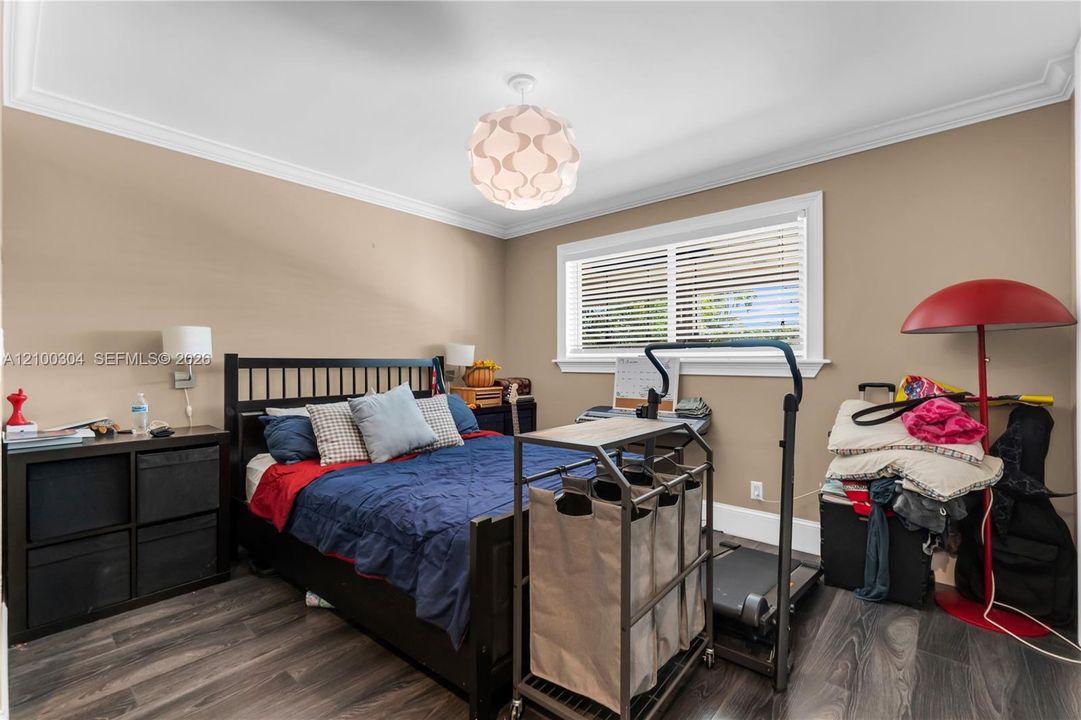 Bedroom featuring crown molding, wood-finish flooring, a contemporary globe-style pendant light fixture, and horizontal window blinds