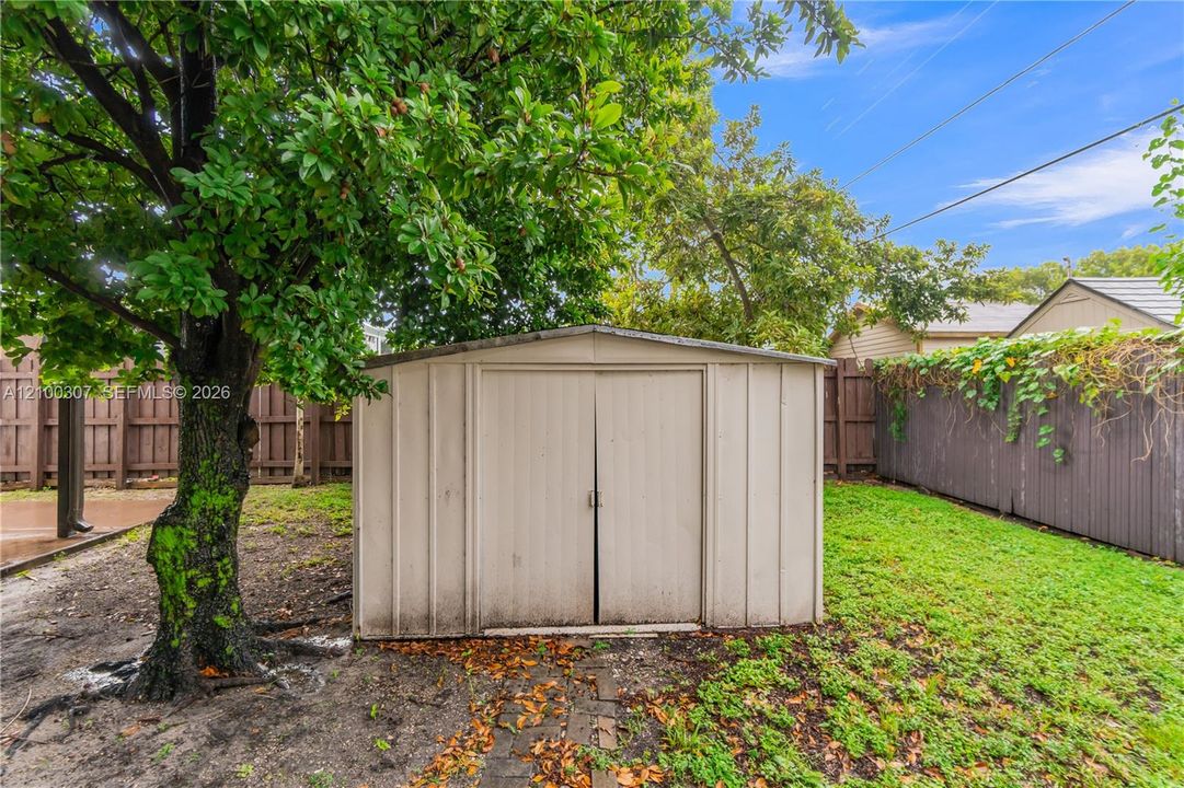 Metal storage shed situated on a lot enclosed by wood privacy fencing and featuring a mature tree
