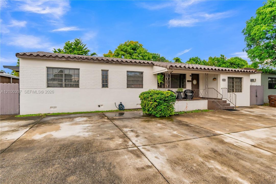 Single-story residence featuring a painted brick exterior, clay tile roof, expansive concrete driveway, covered front porch, and metal decorative railings
