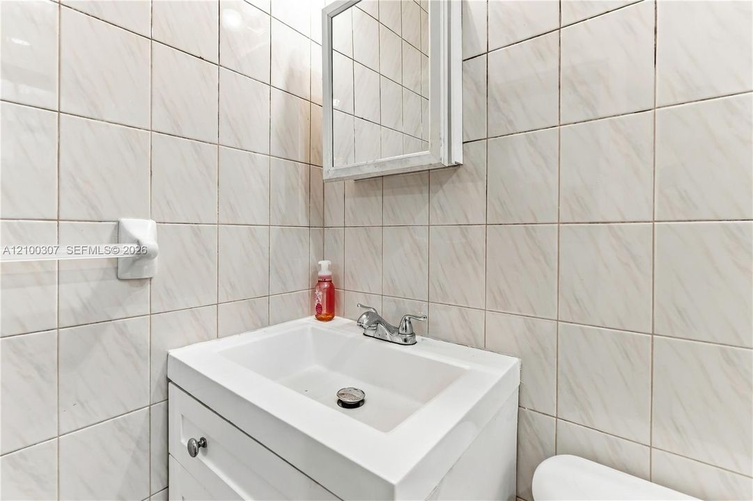 White vanity cabinet featuring a rectangular basin, chrome dual-handle faucet, integrated medicine cabinet, and floor-to-ceiling ceramic tile wall finishes