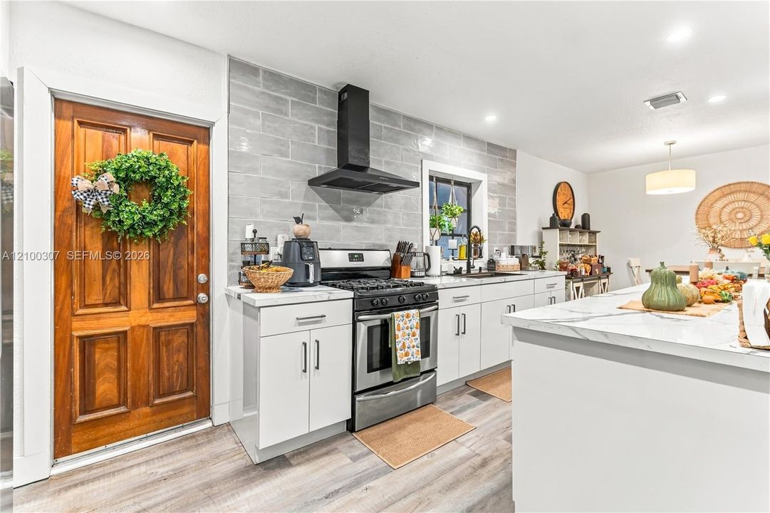 Kitchen featuring white cabinetry, stone-surface island, wood-finish flooring, full-height tile backsplash, and a black chimney-style range hood