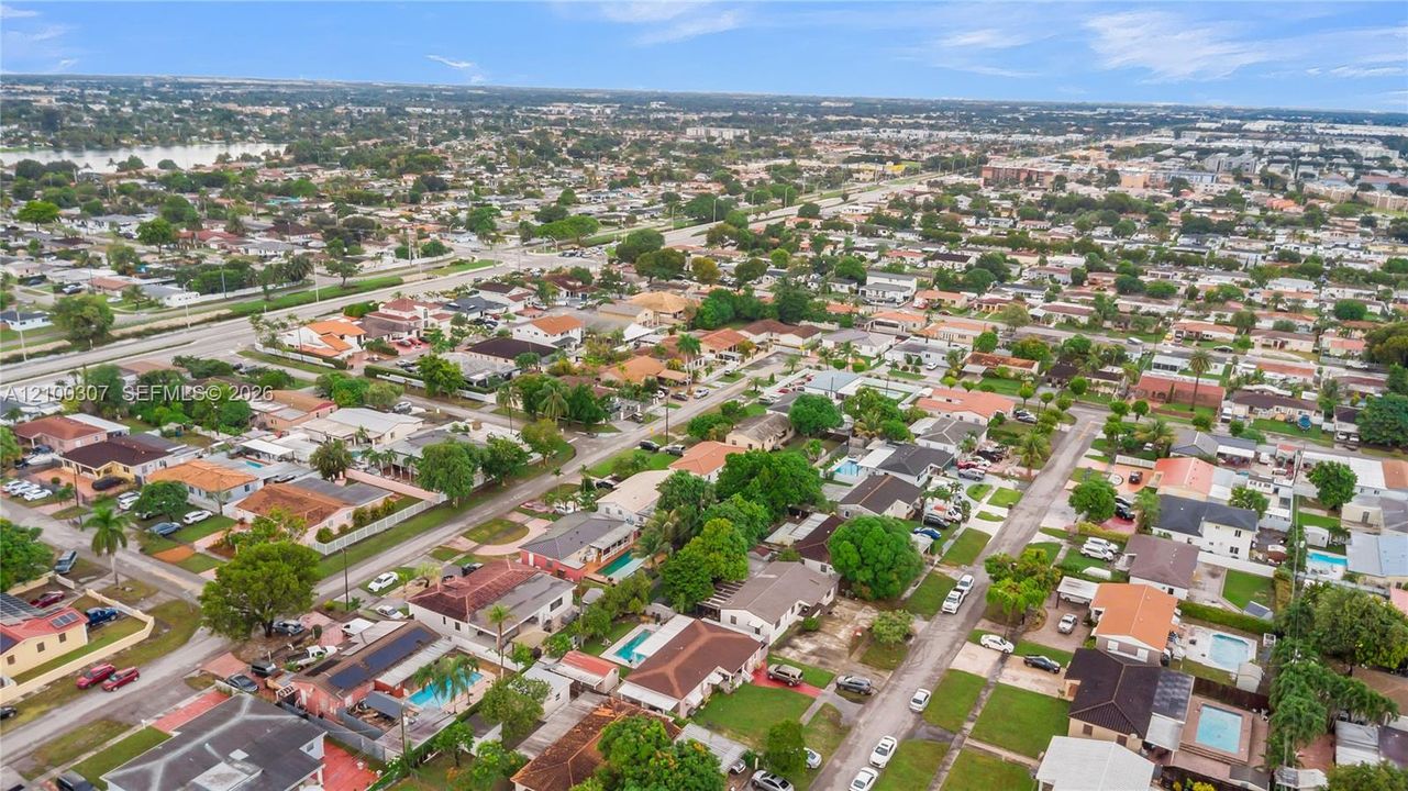 Aerial perspective of a suburban neighborhood featuring residential dwellings, established trees, paved street networks, and residential swimming pools