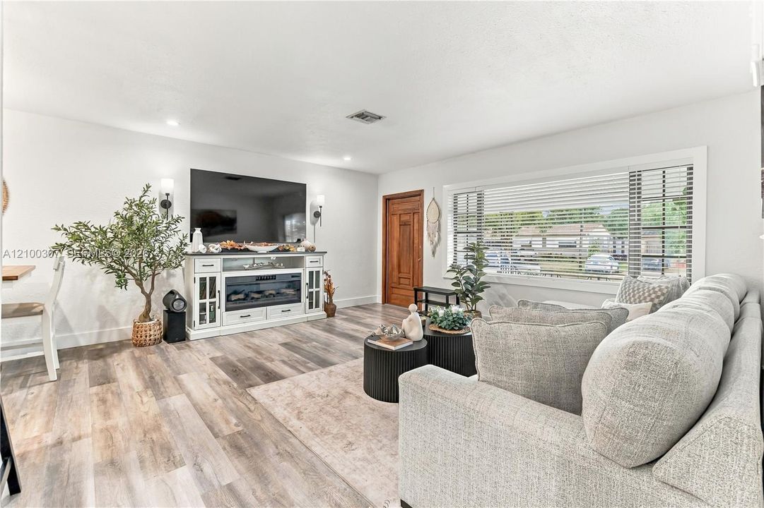 Living area featuring wood-finish flooring, large picture window with blinds, recessed lighting, and a paneled wooden entry door