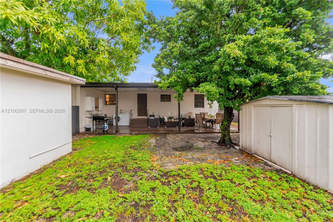 Outdoor living space featuring a covered patio, mature trees, and a detached storage structure