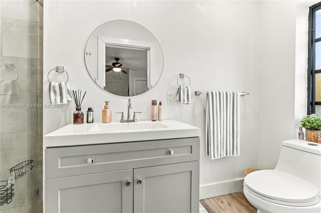 Modern vanity with integrated rectangular sink and quartz-finish countertop, frameless round wall mirror, brushed metal fixtures, and wood-finish flooring