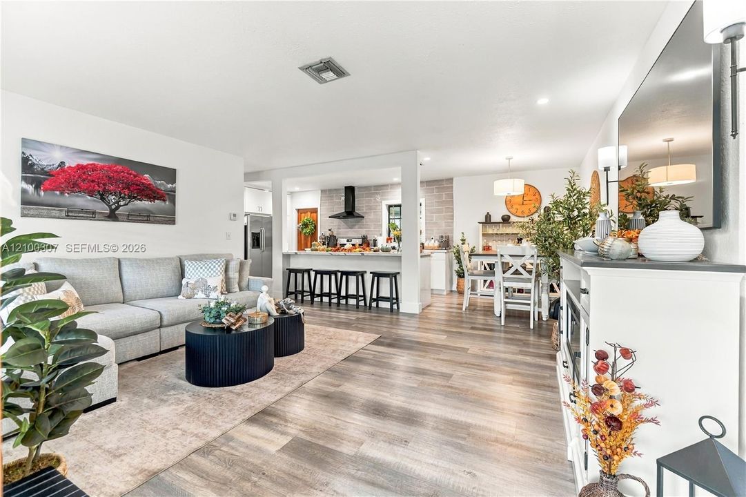 Open-concept living space featuring wood-finish flooring, recessed lighting, a breakfast bar with built-in seating, and a kitchen accented by a stone-style wall and a matte black range hood