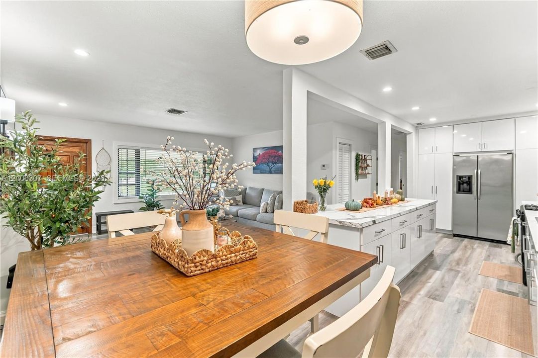 Kitchen featuring white high-gloss cabinetry, stone-finish countertops, stainless steel refrigerator, and wood-finish flooring with a drum-style pendant light fixture
