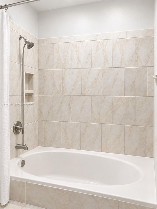 Soaking tub featuring a tiled surround, integrated shower plumbing with a slide bar, and a recessed tiled wall niche