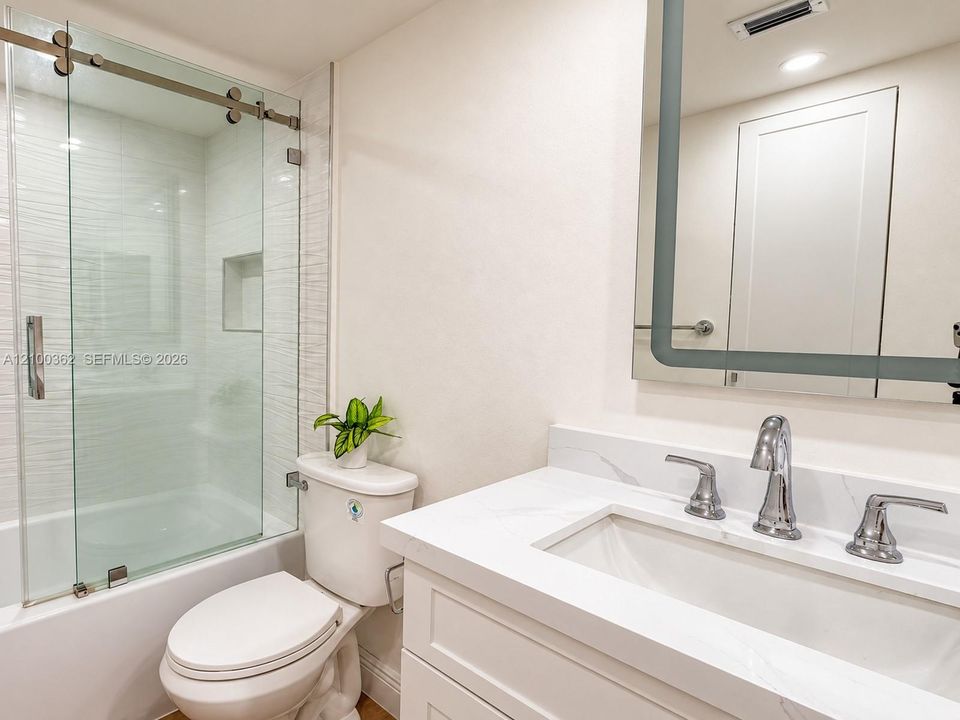 Sleek modern bathroom featuring an LED backlit mirror, stylish white vanity, and glass shower doors.
