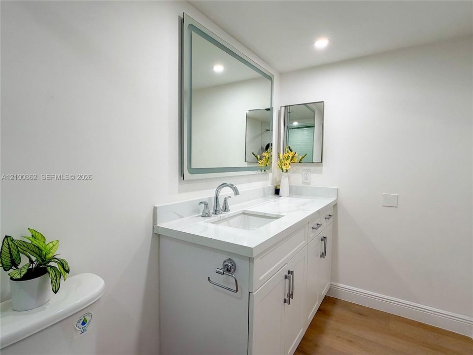 Alternate view of the modern bathroom showcasing the white vanity, clean finishes, and bright LED mirror.