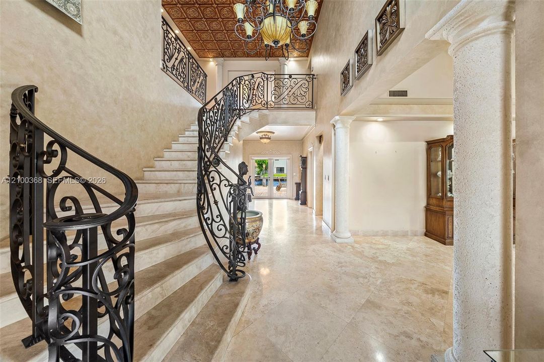 Foyer featuring stone flooring, a decorative patterned ceiling, an ornamental wrought iron staircase railing, and architectural columns