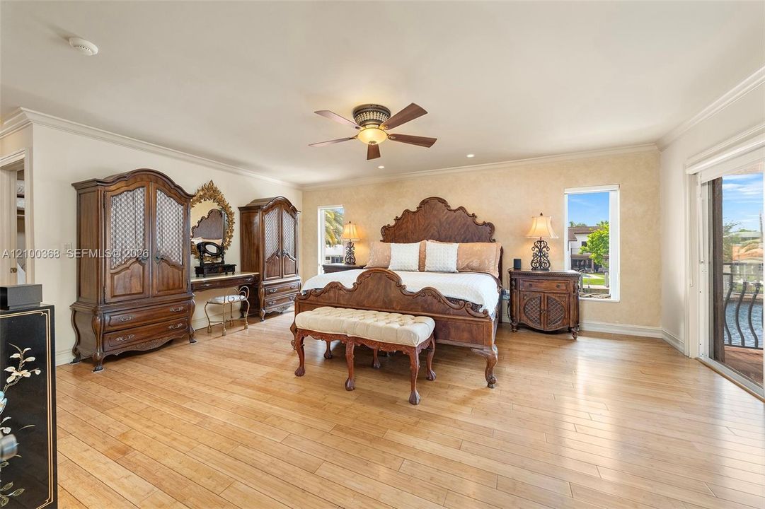 Spacious room featuring wood-finish flooring, crown molding, a central ceiling fan with integrated lighting, and glass sliding doors