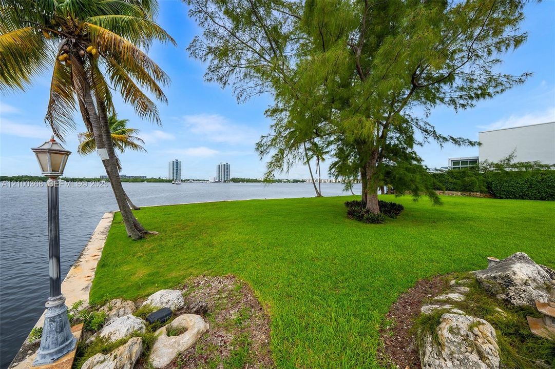 Waterfront lawn featuring mature trees, natural stone accents, and a classic metal post lantern
