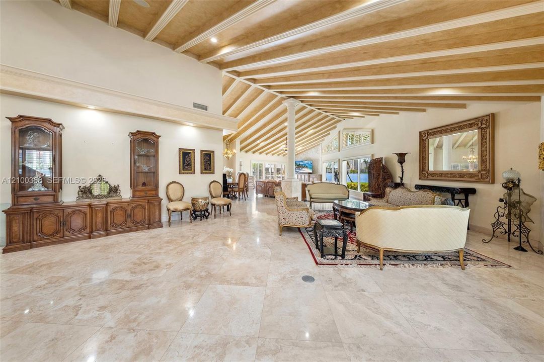 Vaulted ceiling with exposed wood beams, polished stone flooring, and built-in cabinetry featuring glass-front display towers