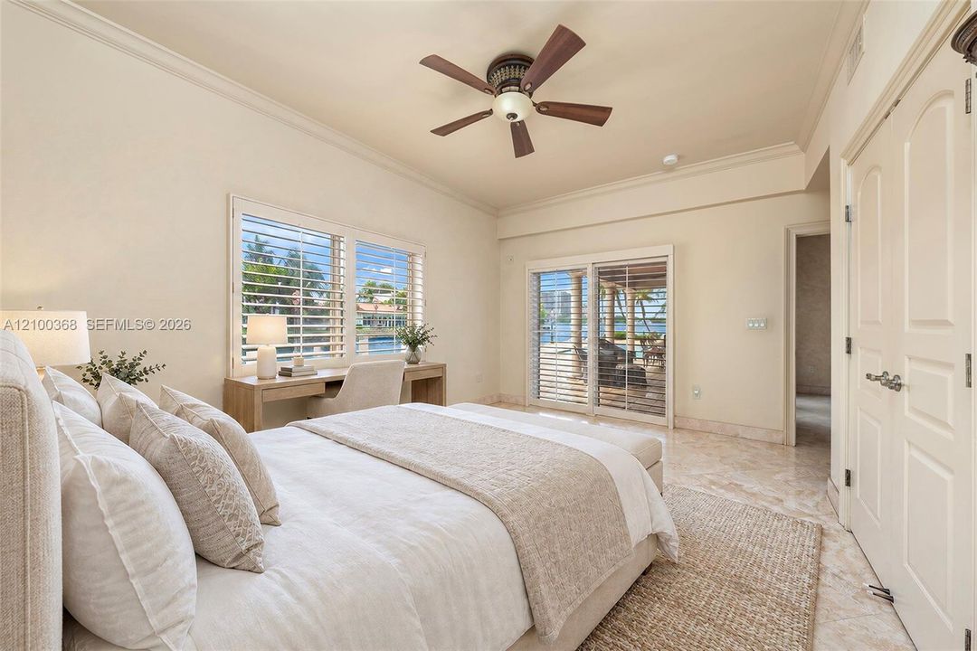 Room featuring stone-finish tile flooring, ceiling fan, crown molding, built-in desk, and sliding glass doors
