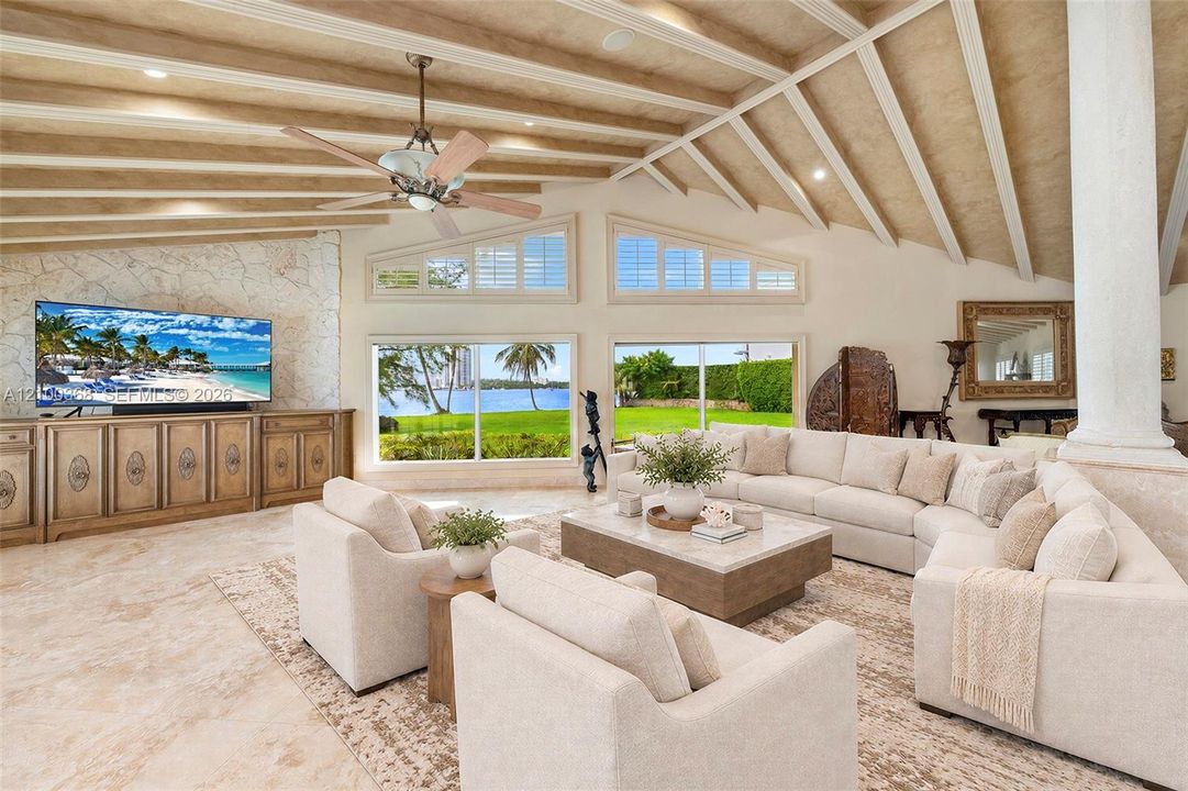 Vaulted ceiling with exposed beams, stone-clad accent wall, oversized windows with window shutters, built-in cabinetry, and stone-finish flooring