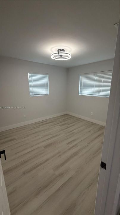 Interior room featuring wood-finish flooring, neutral walls, two windows with horizontal blinds, and a contemporary circular LED ceiling light fixture