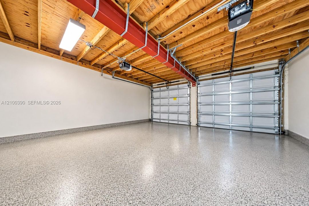 Two-car garage featuring an exposed wood-joist ceiling, industrial red steel support beam, durable epoxy-coated flooring, and dual overhead sectional garage doors