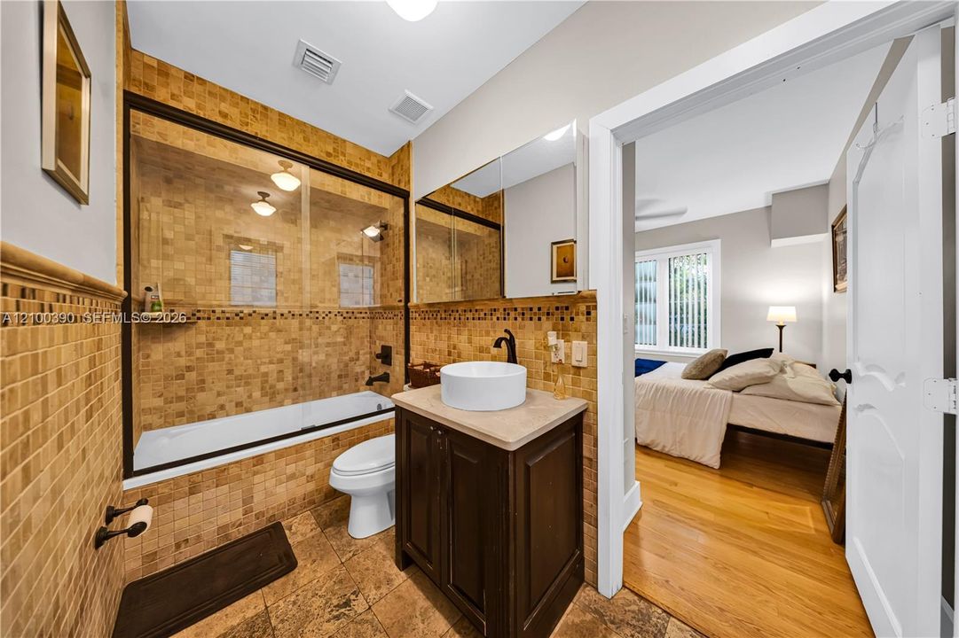 Bathroom featuring mosaic tile wall accents, a glass-enclosed bathtub, a vanity with a stone countertop and white vessel sink, and oil-rubbed bronze plumbing fixtures