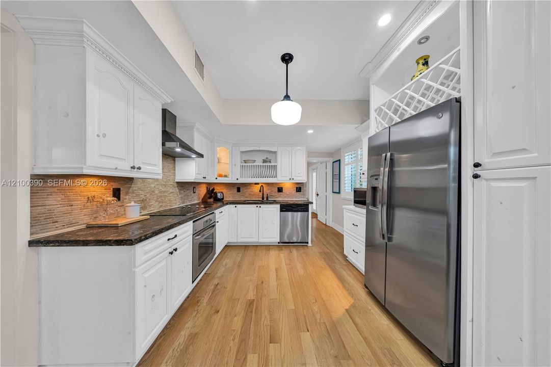 Kitchen featuring white cabinetry, stone-surface countertops, stone tile backsplash, stainless steel appliances, and wood-finish flooring