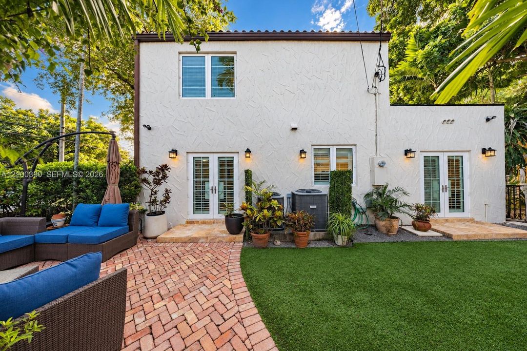 Stucco exterior featuring dual sets of French doors, brick paver patio, and synthetic turf lawn