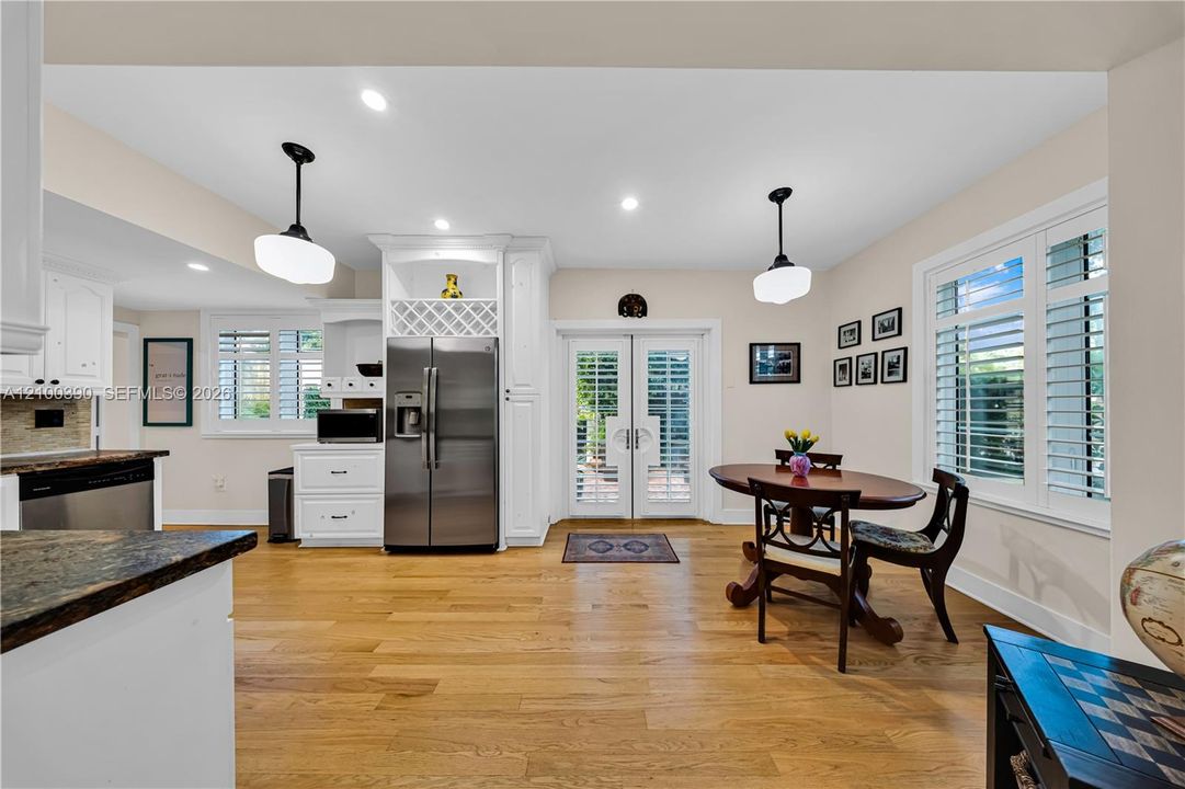 Kitchen featuring wood-finish flooring, white cabinetry with integrated wine storage, stainless steel appliances, dual pendant lighting, and French doors with plantation shutters