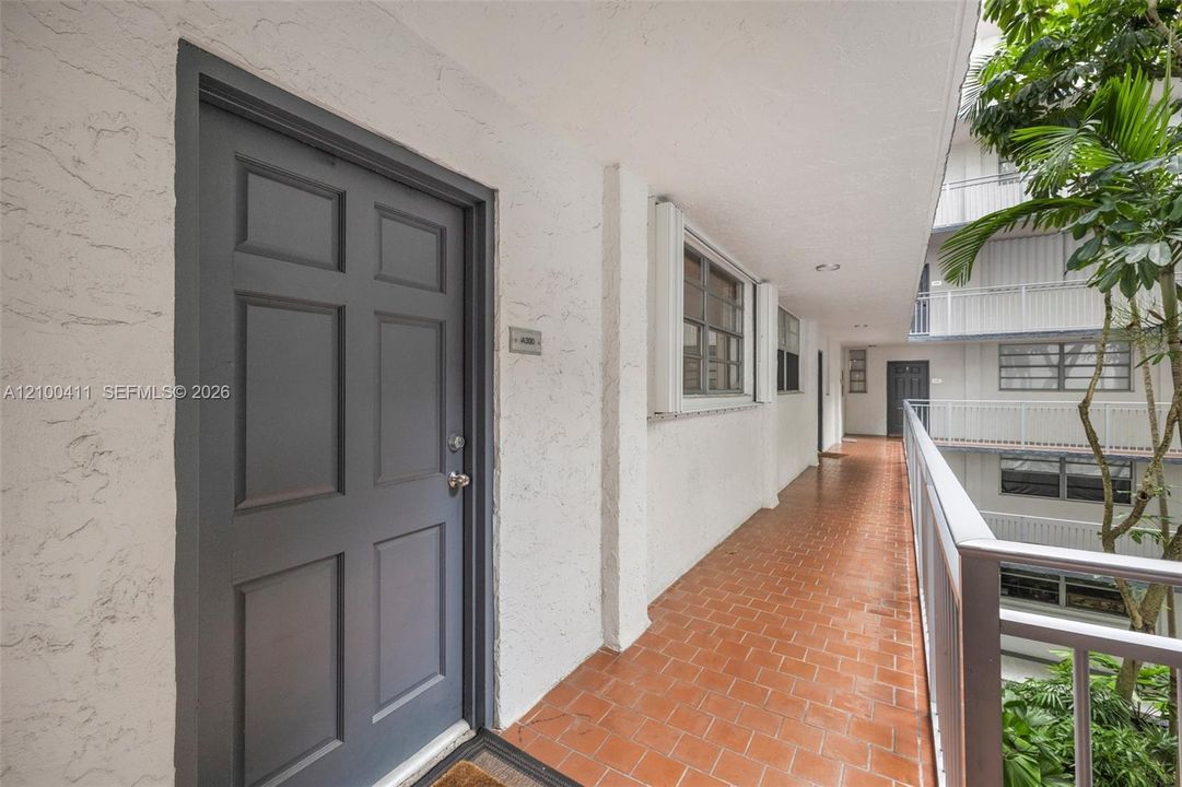 Exterior entryway featuring a textured stucco facade, a six-panel door, terracotta tile flooring, and a metal railing