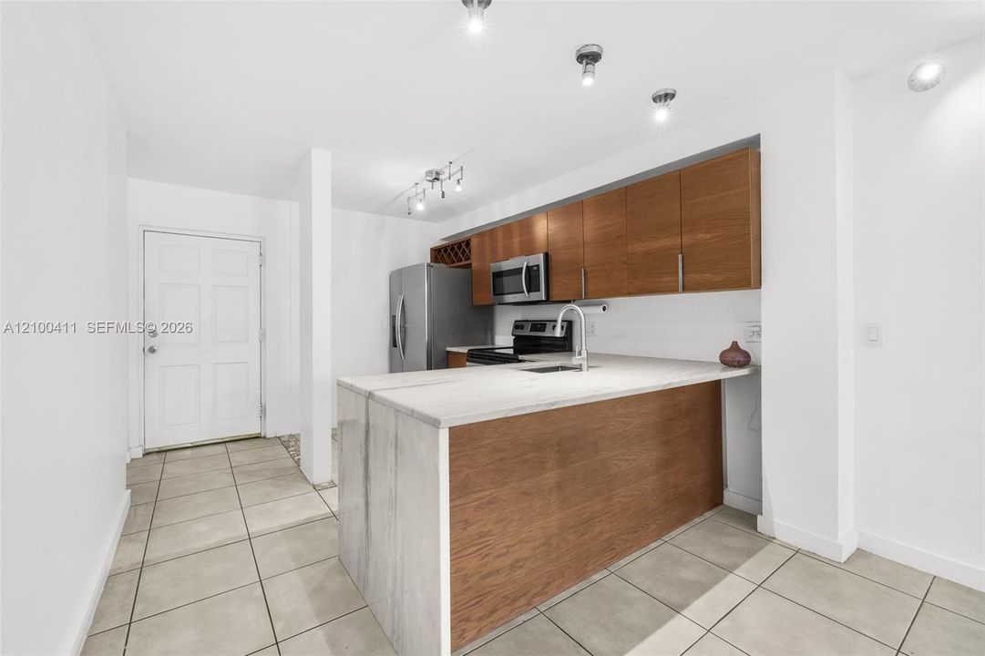 Kitchen featuring flat-panel wood-finish cabinetry, stainless steel appliances, stone-surface peninsula, and tile flooring