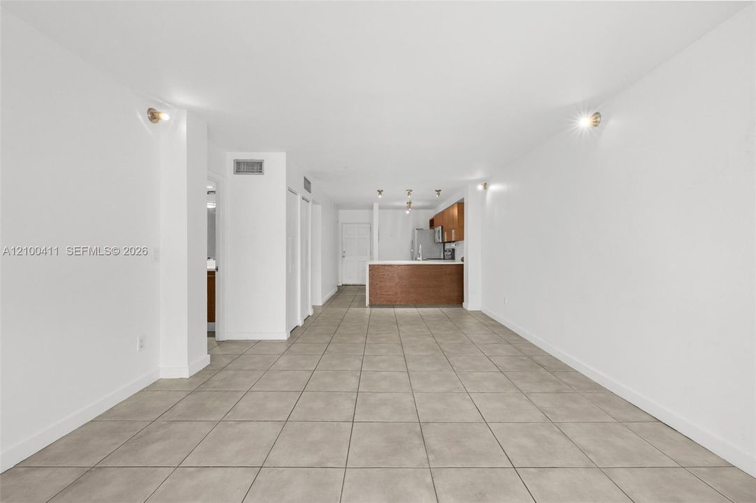 Neutral-toned tile flooring throughout the open-concept interior, featuring wall-mounted lighting fixtures, a kitchen peninsula with wood-finish cabinetry, and recessed lighting