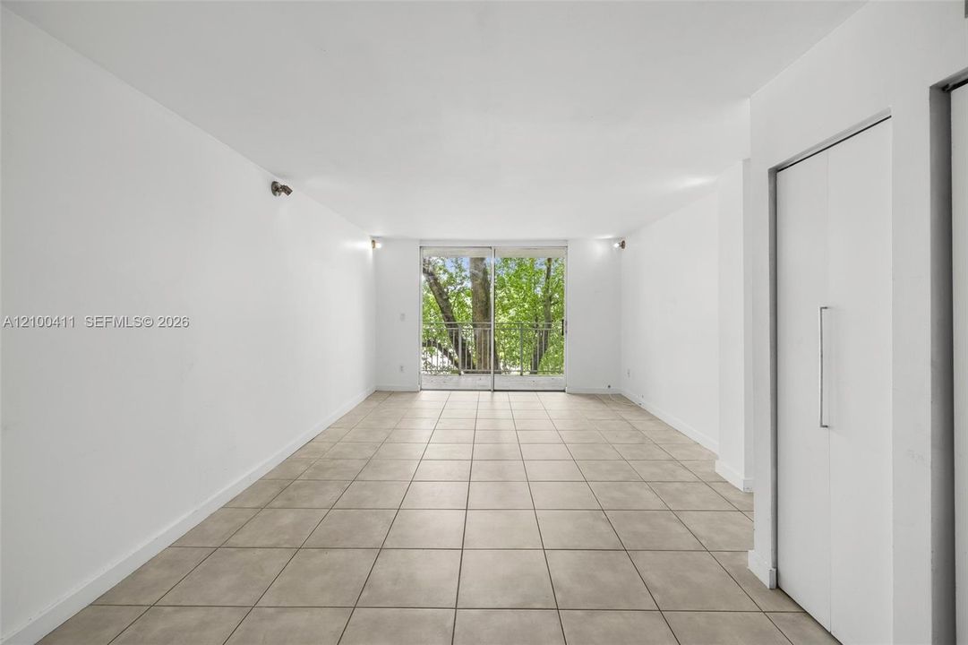Open-concept space featuring large-format ceramic tile flooring, built-in floor-to-ceiling cabinetry, sliding glass doors, and a metal balcony railing