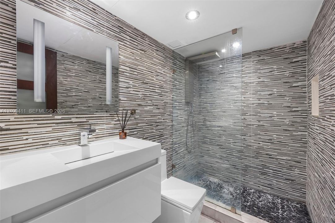 Modern floating vanity with a seamless integrated sink, wall-mounted faucet, linear multi-toned tile wall covering, frameless glass shower enclosure, and recessed shower shelving