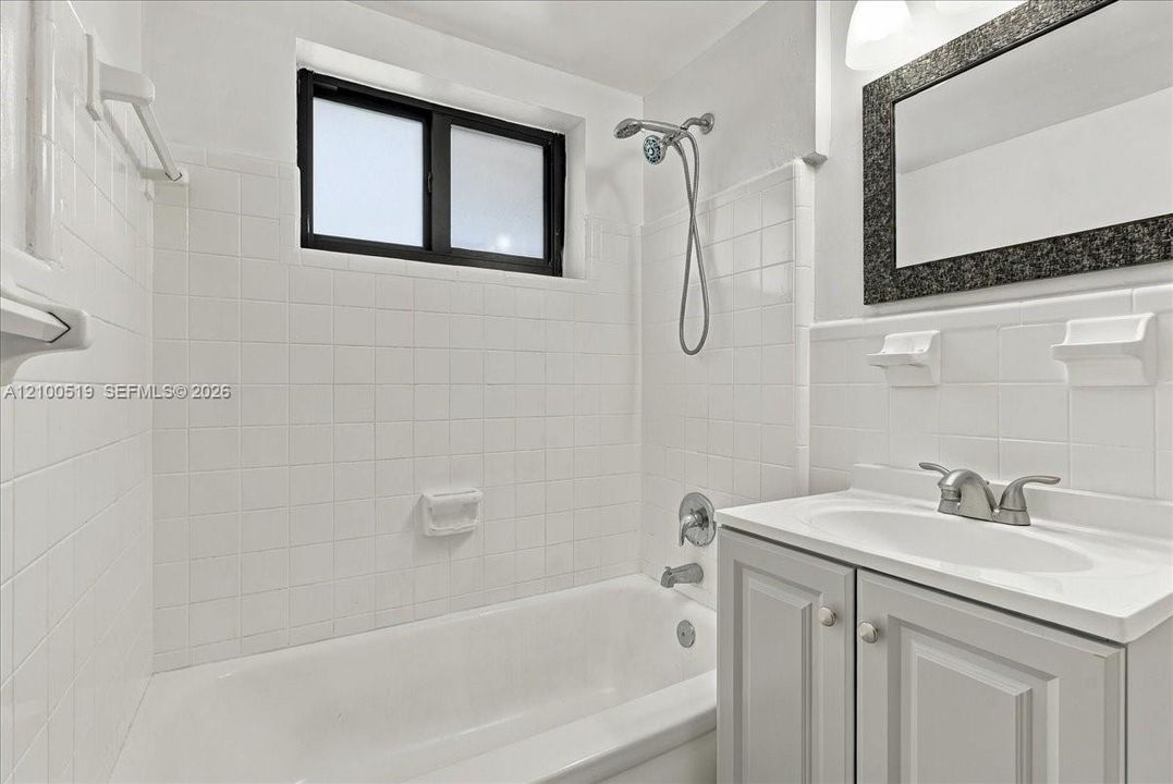 Full bathroom featuring white wall tiling, a combination tub and shower with a handheld fixture, vanity with a solid-surface top, and a framed mirror