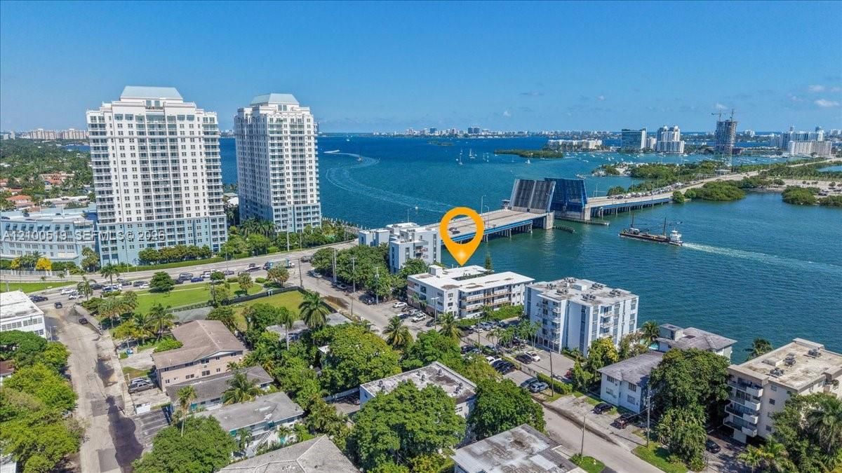 Aerial perspective of coastal multi-story residential building featuring proximity to waterfront, bridge access, and mature landscaping