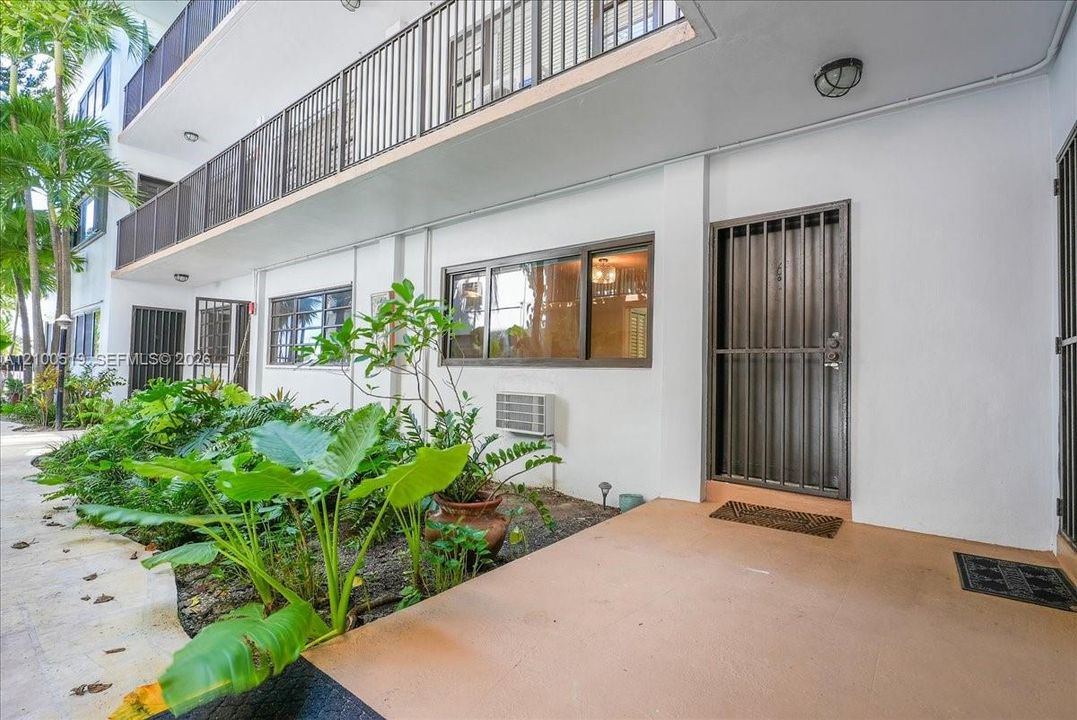 Ground-level exterior entry featuring a covered porch, metal security door, dual-pane windows, and landscaped garden border