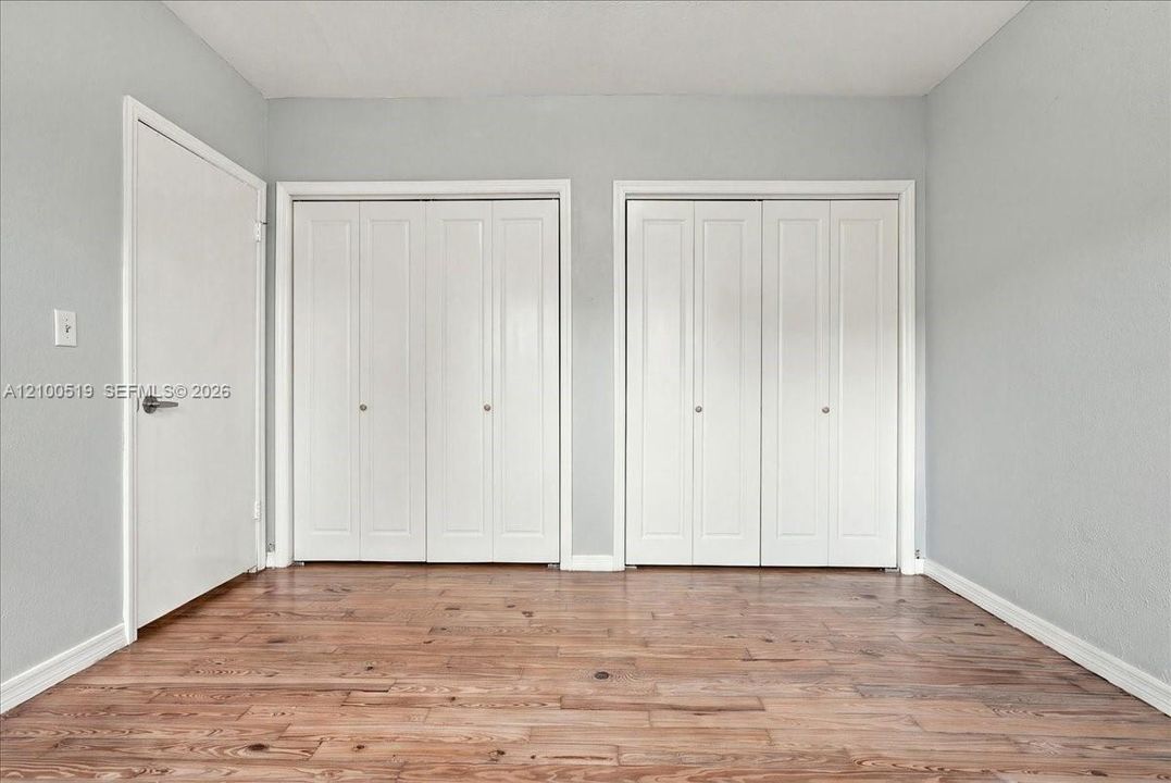 Room featuring wood-finish flooring, two sets of white bi-fold closet doors, and a solid-core interior door