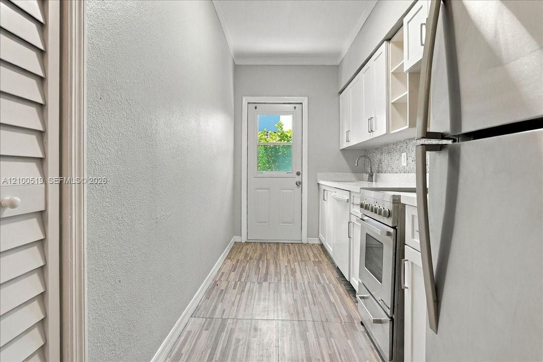 Kitchen featuring white shaker-style cabinetry, wood-finish flooring, stainless steel range, and mosaic-style tiled backsplash