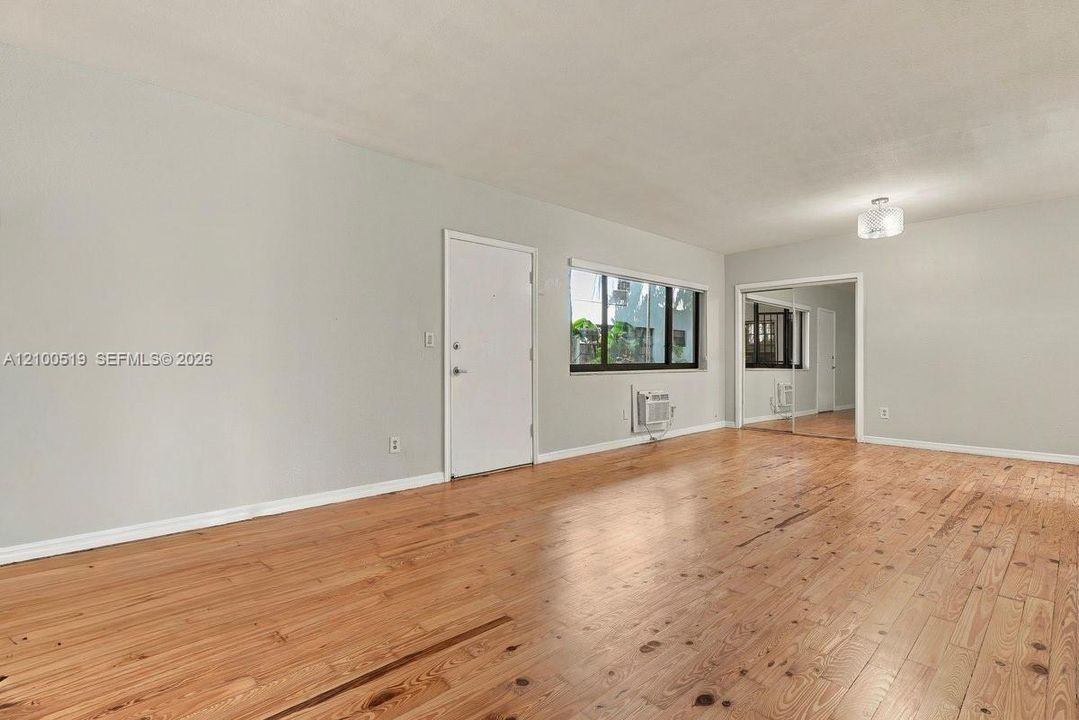Wood-finish flooring, neutral wall tones, large window, sliding mirrored closet doors, and flush-mount ceiling lighting