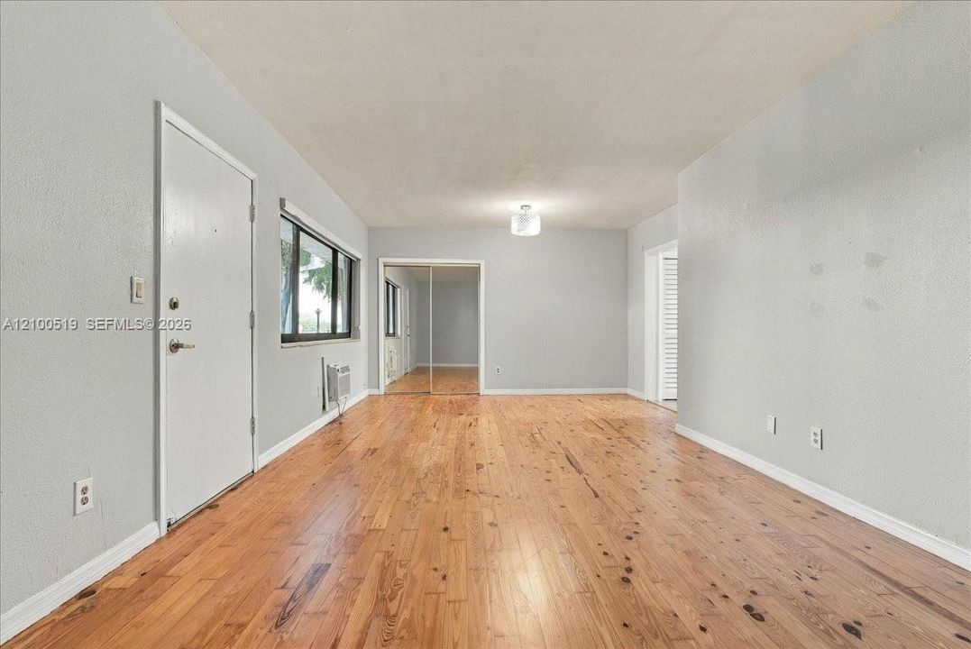 Interior space featuring wood-finish flooring, light gray walls, a flush-mount ceiling light fixture, and floor-to-ceiling mirrored closet doors